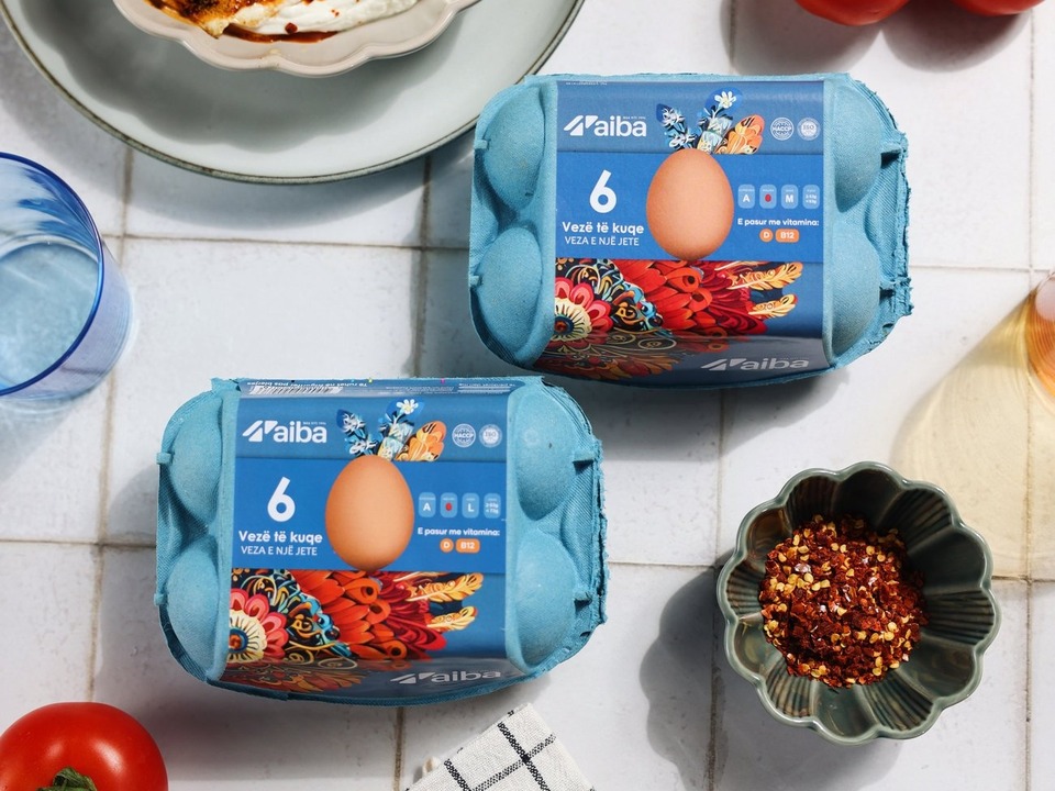 Two blue AIBA egg cartons on white tiles with chilli flakes and a fried egg