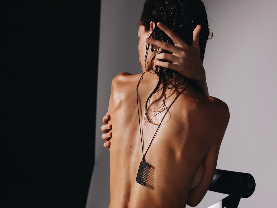 Model seen from behind with one hand in her wet hair, wearing the Bannu comb pendant