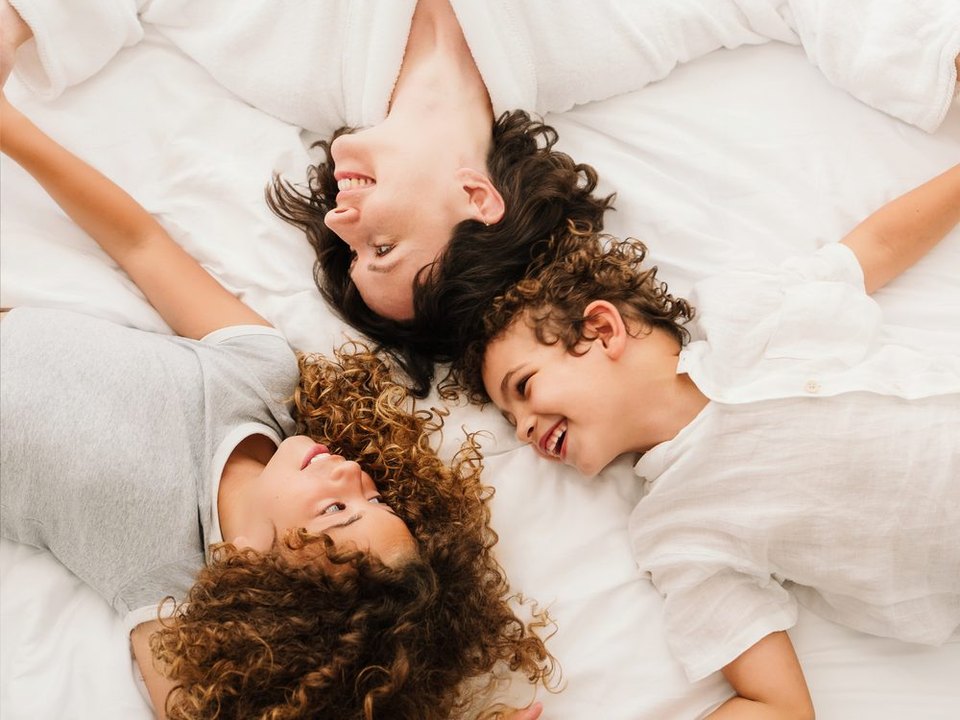 Mother and two children laughing on a white Mövenpick bed